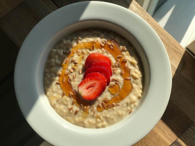 Porridge chaud aux fraises fraiches et graines de lin dorées dans un bol blanc